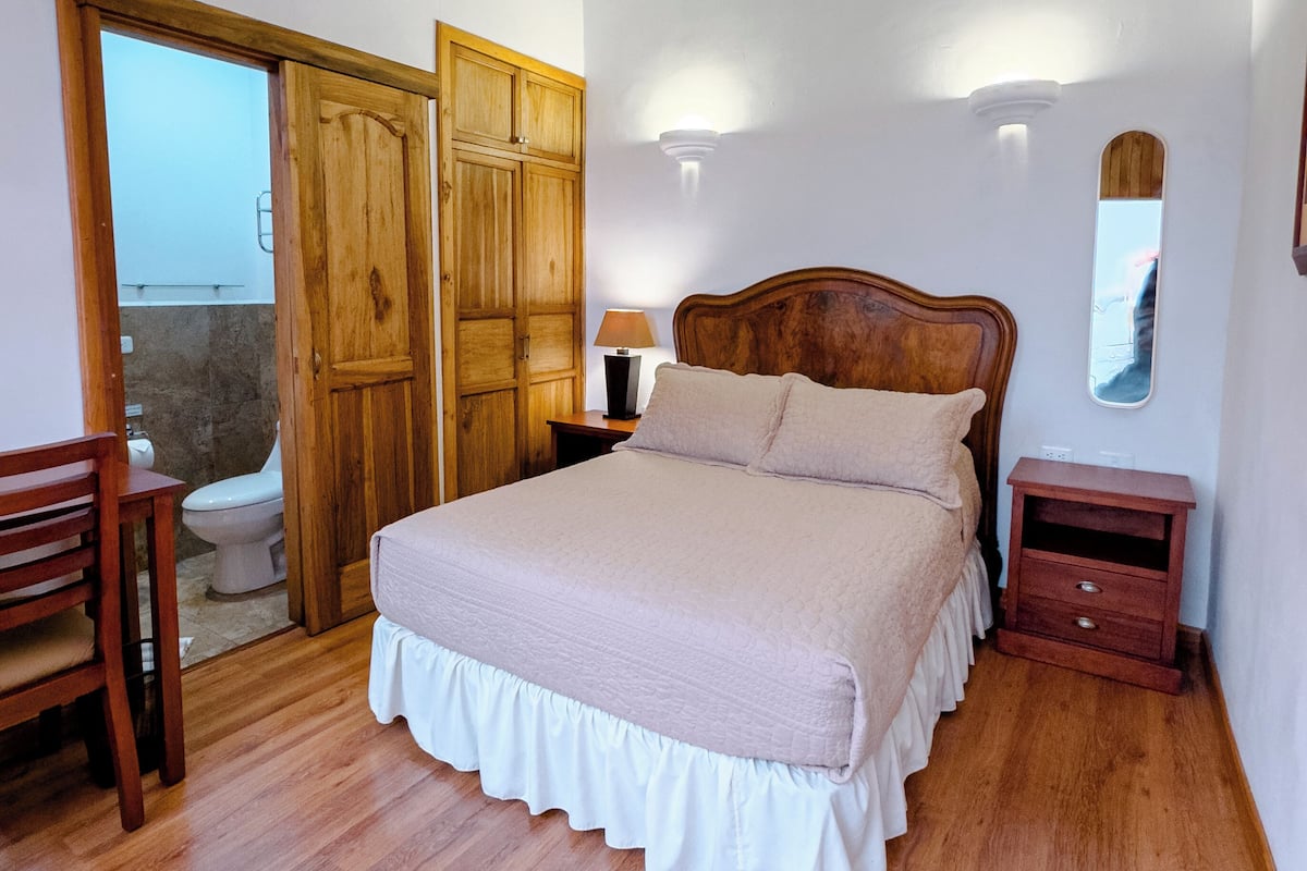A bedroom with a wooden bed, a nightstand, a chair, and a wooden wardrobe.