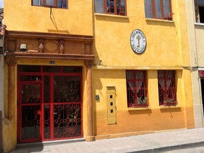 Un edificio amarillo con puerta roja y ventanas, una placa que dice 'Casa Montalt', y una pequeña ventana con una planta en maceta.