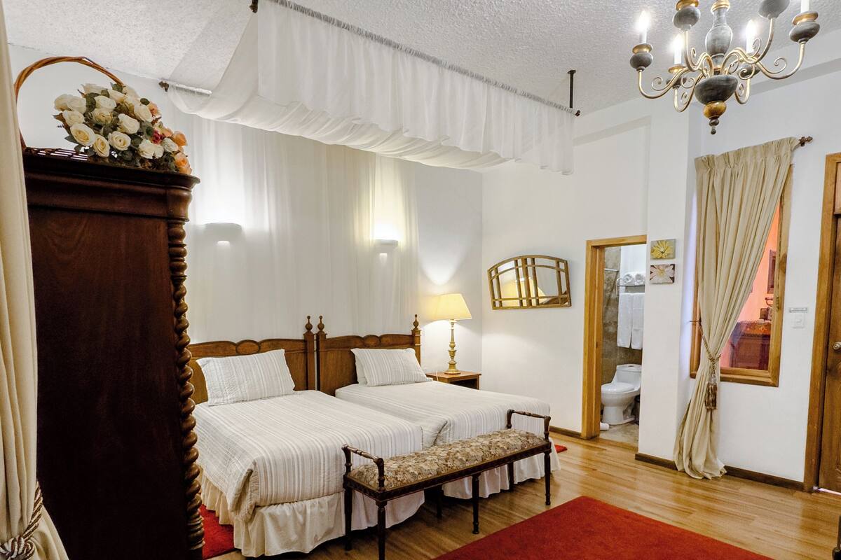 A bedroom with two beds, a wooden wardrobe, a red rug, and a chandelier.