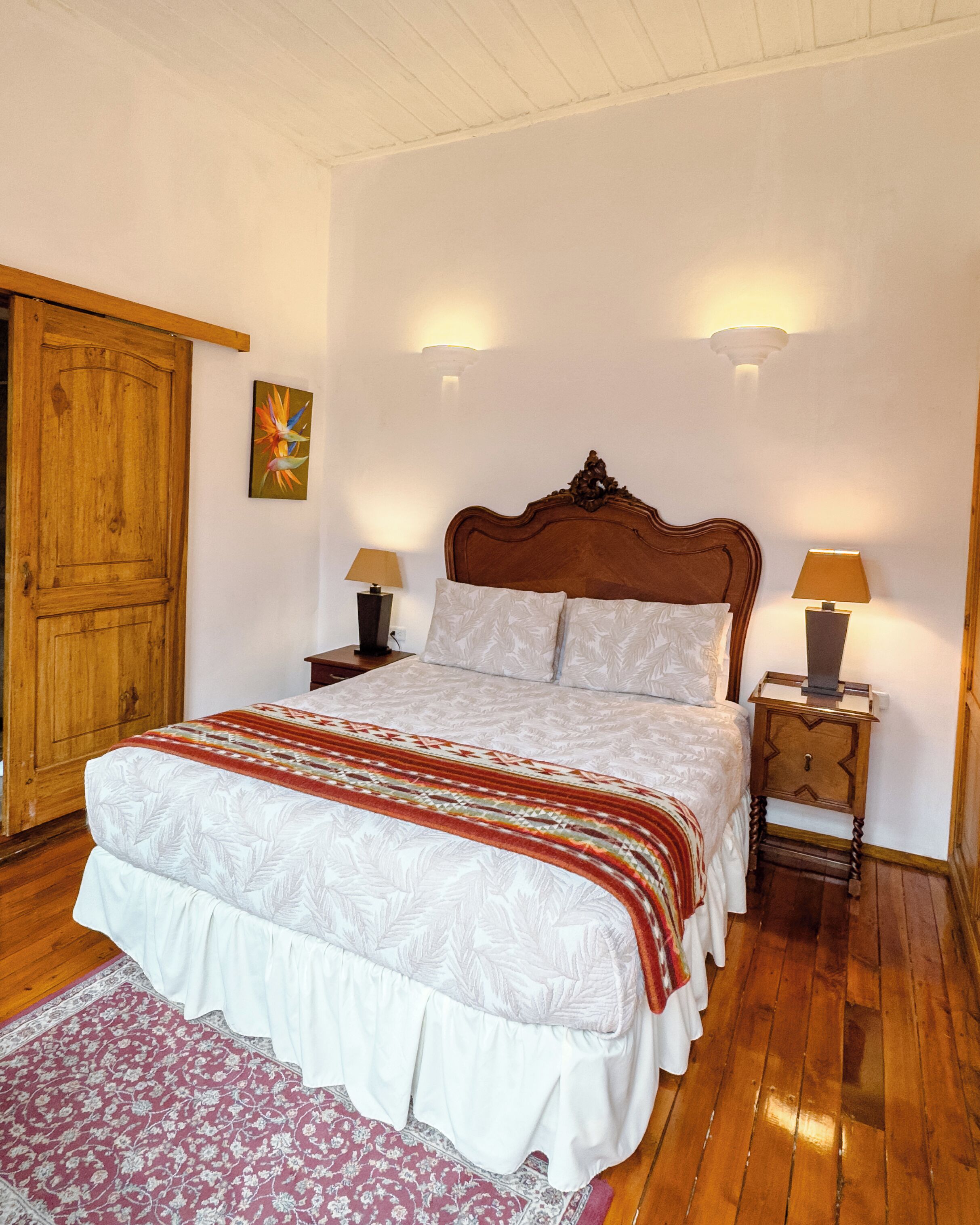 A bedroom with a wooden bed, two bedside tables with lamps, a wooden wardrobe, and a floral rug.