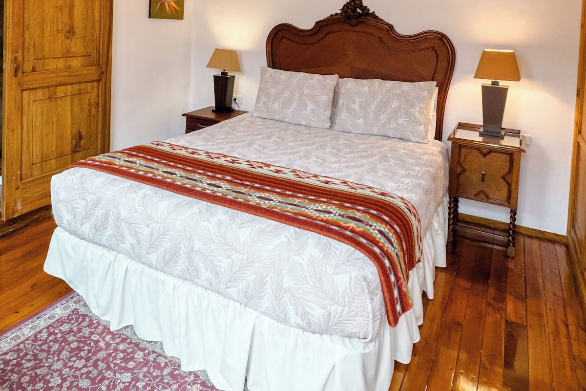 A bedroom with a wooden bed, two bedside tables with lamps, a wooden wardrobe, and a floral rug.