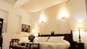 A bedroom with a bed, bedside lamps, a nightstand, a chair, a table with a vase, and a painting on the wall. - Hotel Boutique Casa Montalvo Cuenca (Cuenca)