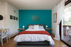 A bedroom with a bed, two bedside tables, a chair, and a view of the outdoors. - Pueblo Canyon Inn (Los Alamos)
