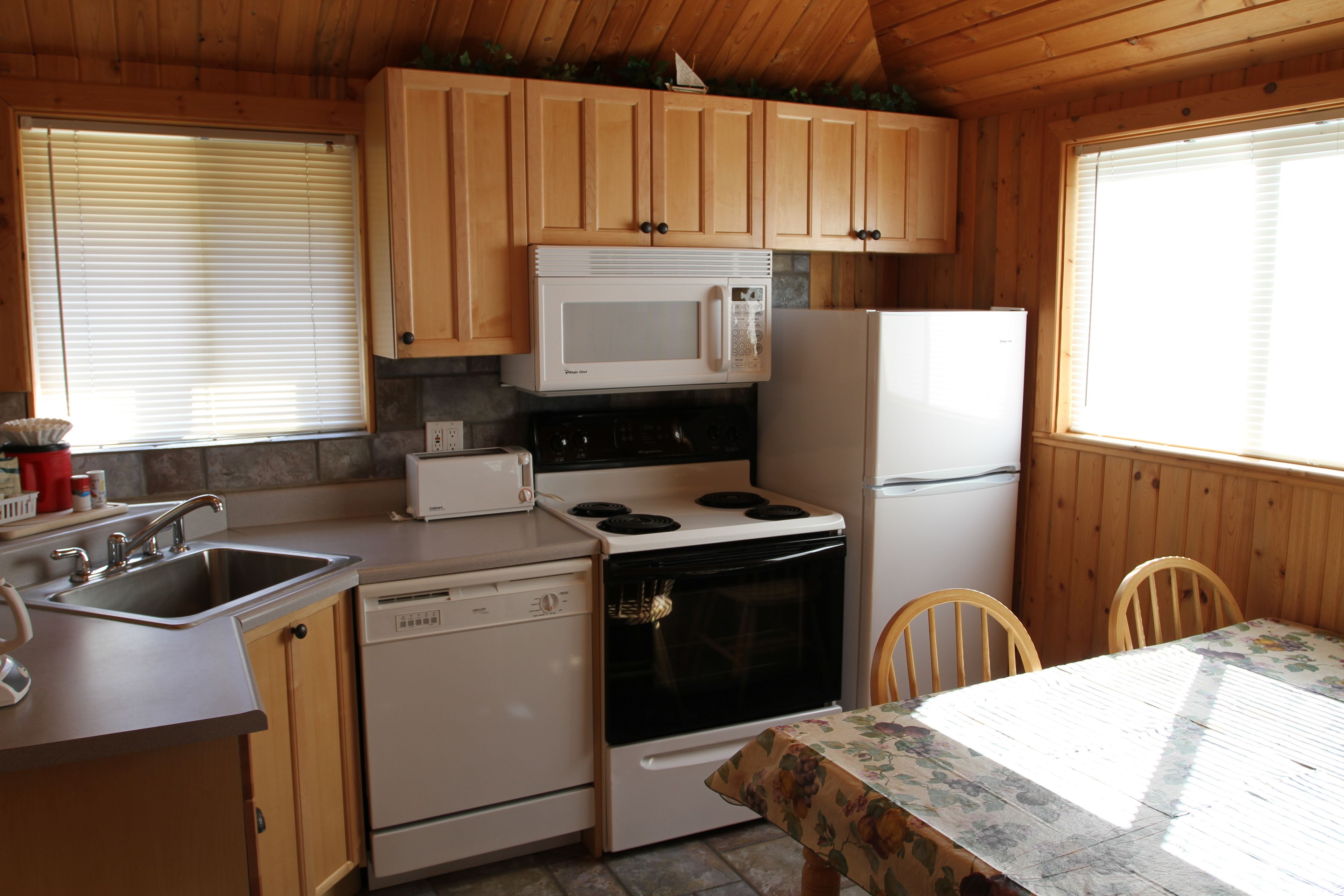 A compact kitchen with wooden cabinets, a microwave, a stove, a refrigerator, a sink, and a table with chairs.