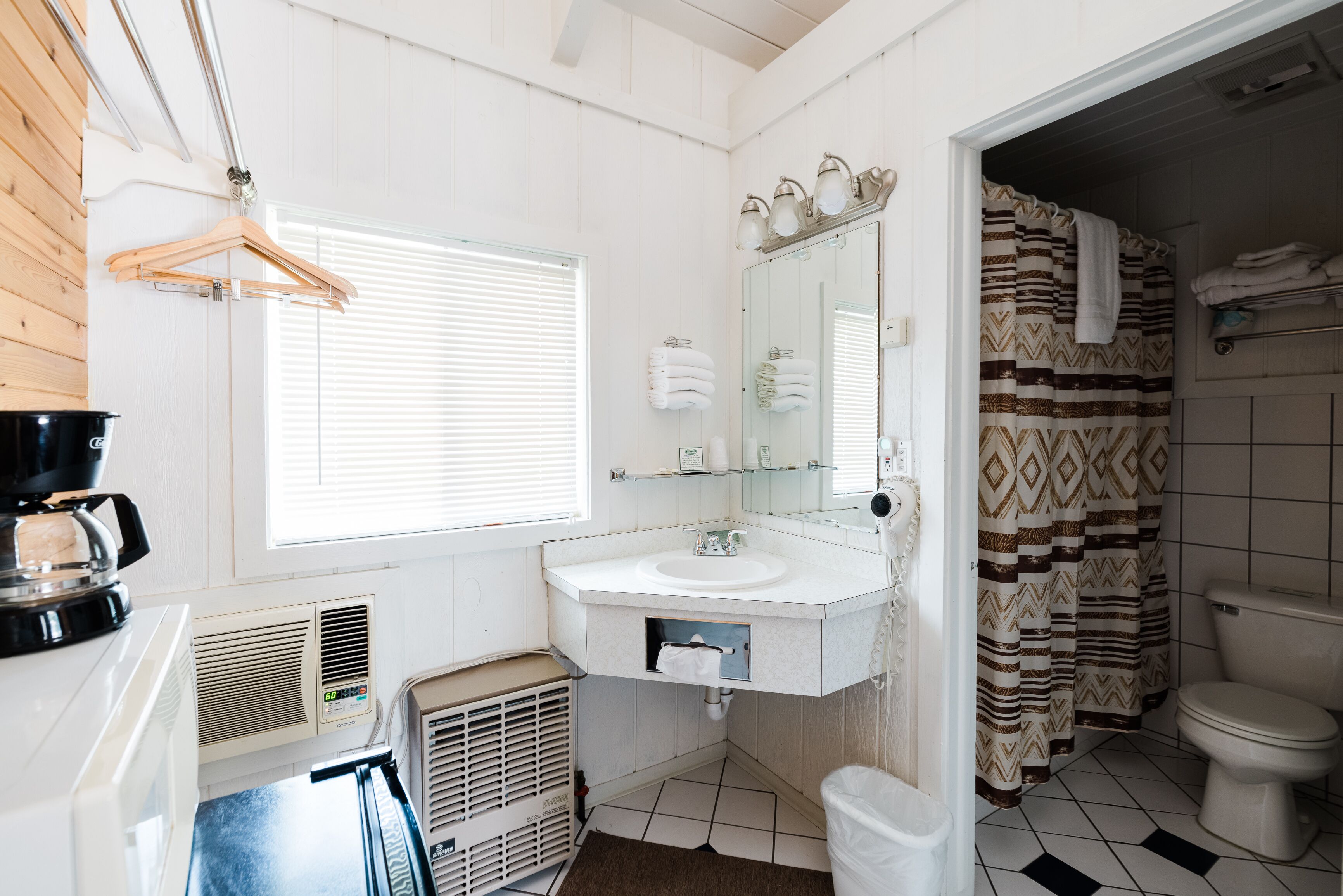 A bathroom with a white sink, mirror, and towel rack. There is a window with blinds, a shower curtain, and a toilet.