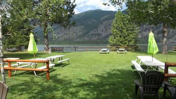 Un espace pique-nique équipé de tables et de chaises, entouré d’une clôture en bois, et offrant une vue sur un lac et des montagnes.