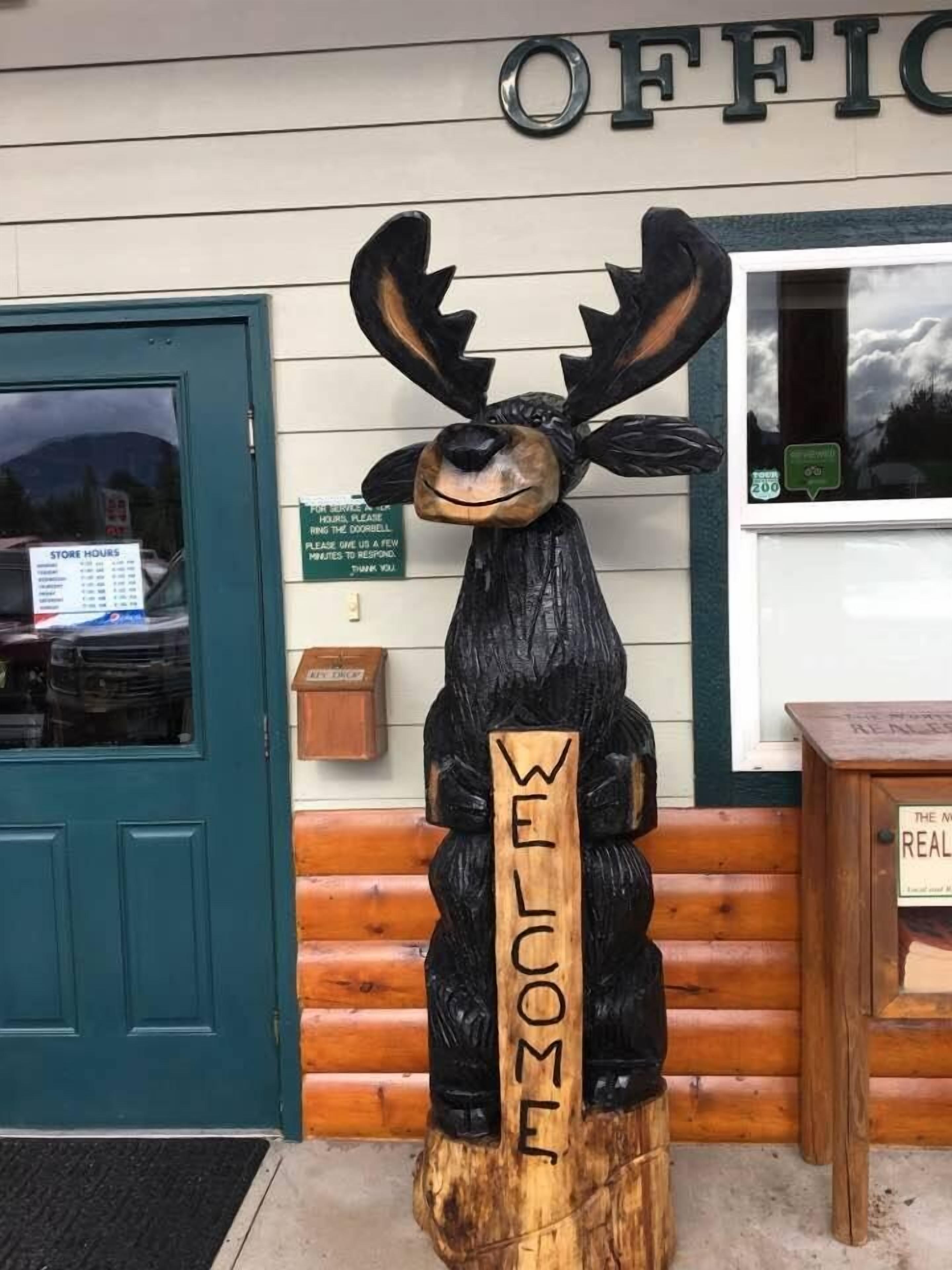 A wooden sign with "WELCOME" carved on it, placed in front of a building with a sign that reads "OFFICE".