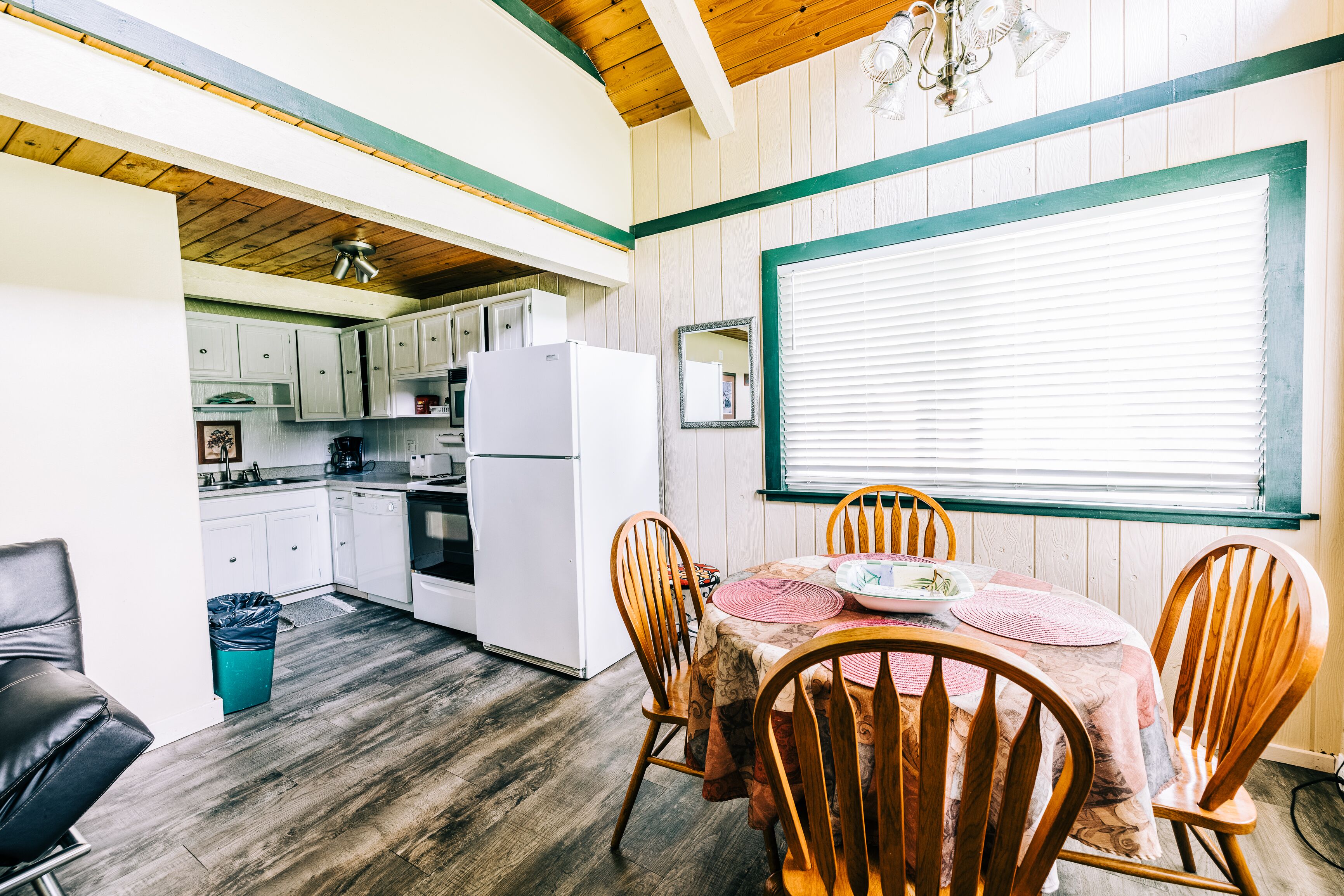 Una cocina compacta con armarios blancos, un refrigerador y una zona de comedor con sillas y una mesa de madera.