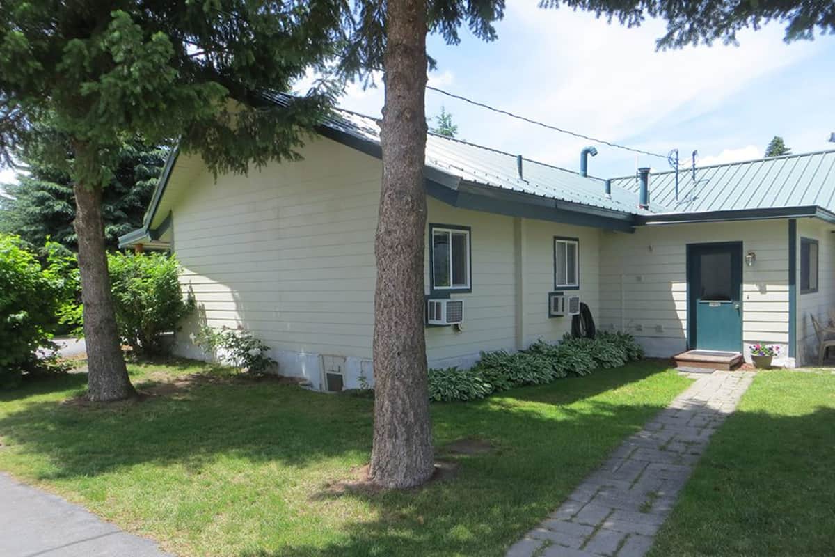 Uma casa térrea com porta verde, um pequeno alpendre e entrada com calçada.