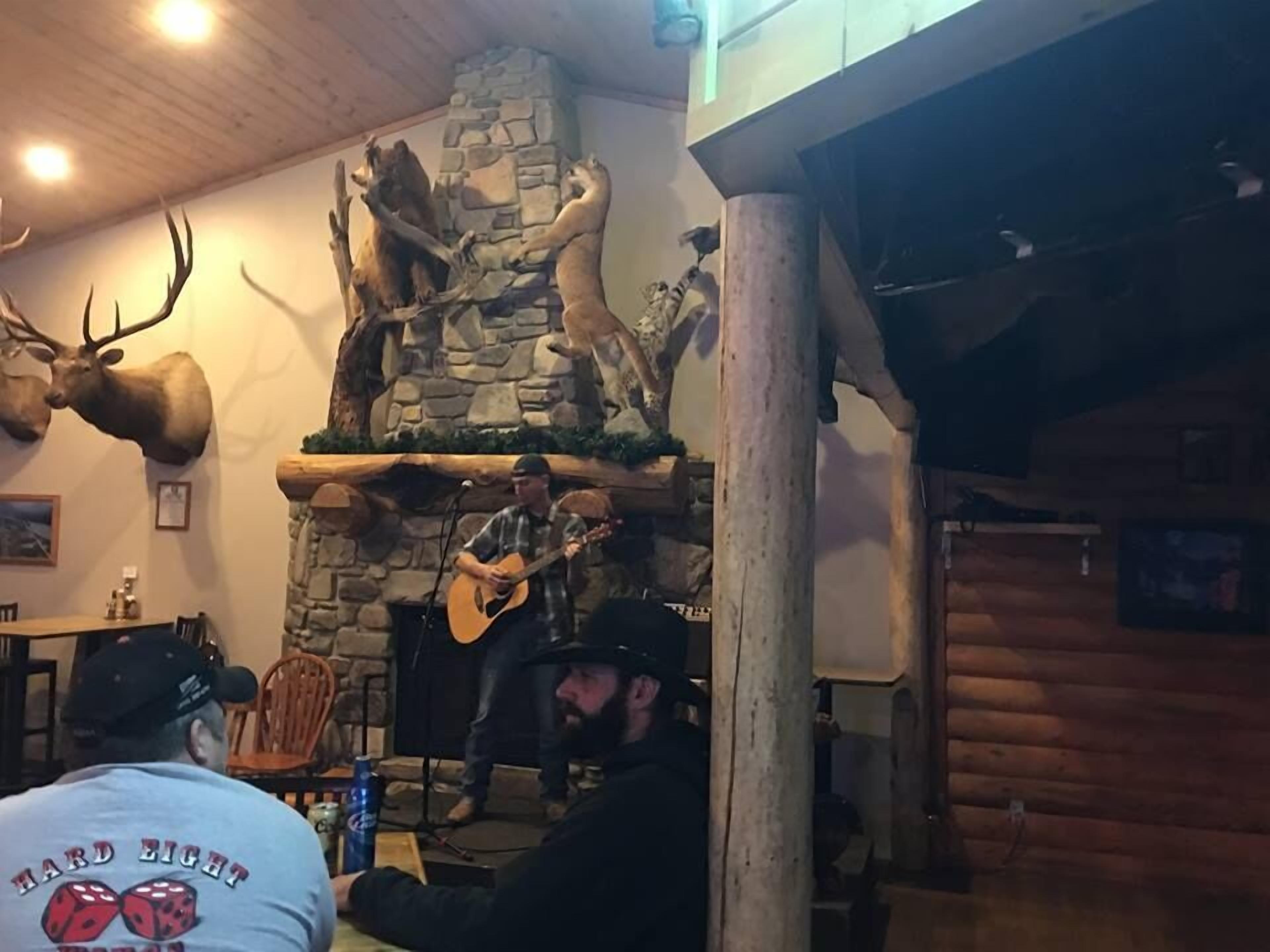 A rustic interior with a stone fireplace, mounted animal heads, and a musician performing.