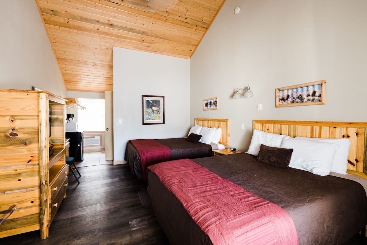Quarto com duas camas, cabeceiras de madeira, um aparador de madeira e uma escrivaninha pequena com cadeira.