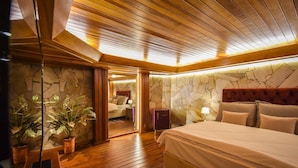 A bedroom with a wooden floor, a bed with a headboard, a nightstand, a dresser, and a stone wall. - Pousada Borô (Gramado)