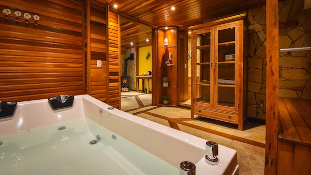 A wooden interior with a large bathtub, a stone wall, and a wooden door leading to another room. - Pousada Borô (Gramado)