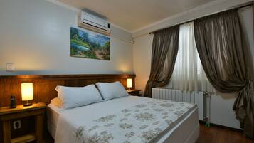 Una habitación de hotel con cama, mesita de noche, aire acondicionado, un cuadro y cortinas.
