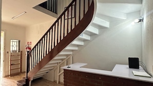 Une pièce spacieuse avec un escalier en bois, un comptoir d’accueil blanc et un mur décoratif en briques.