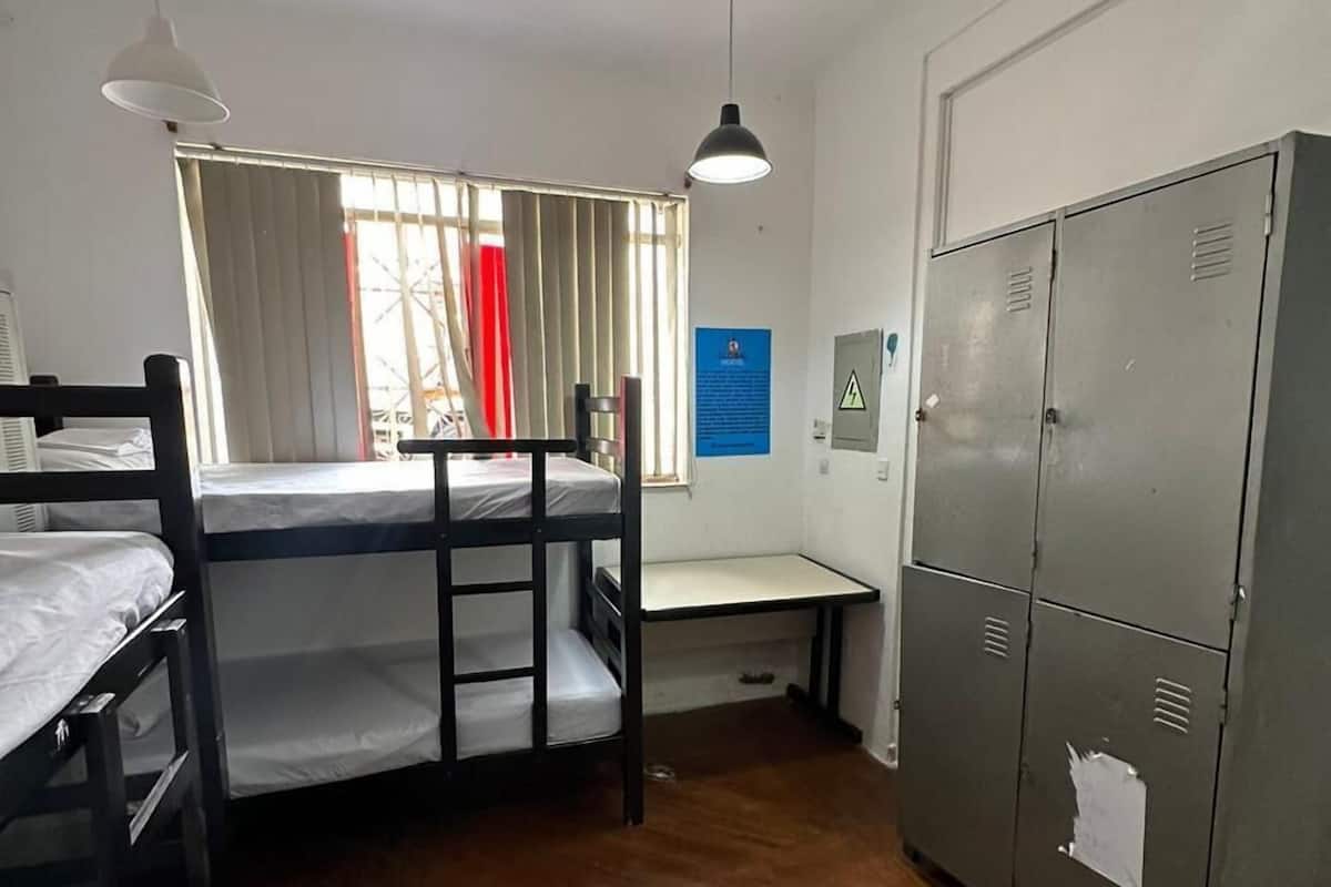 Ein Schlafsaalzimmer mit Etagenbetten, einem Schreibtisch, einem Stuhl, einem Kleiderschrank und einem Fenster mit Vorhängen.