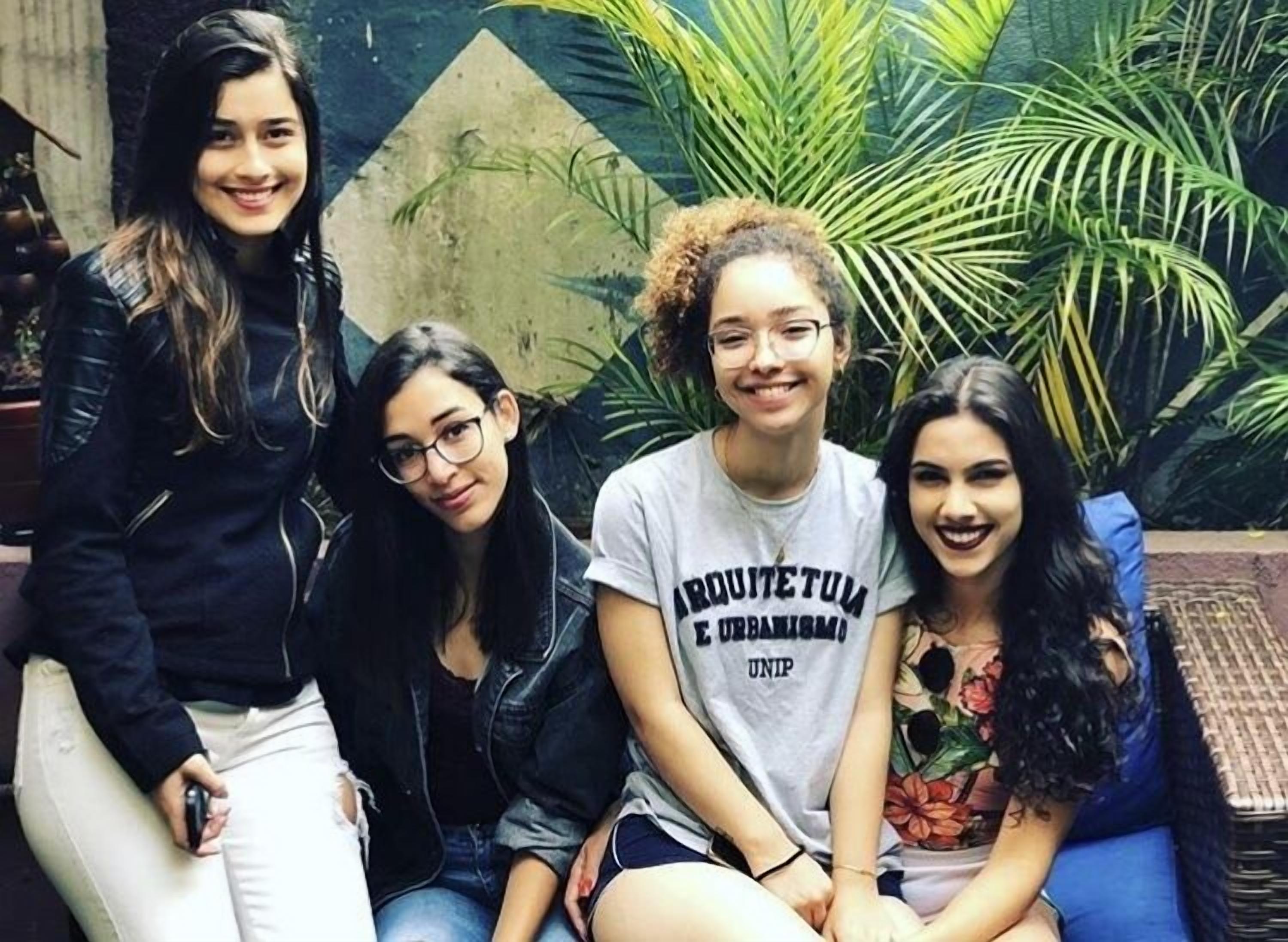 A group of people seated on a couch with a backdrop of green plants and a geometric wall design.