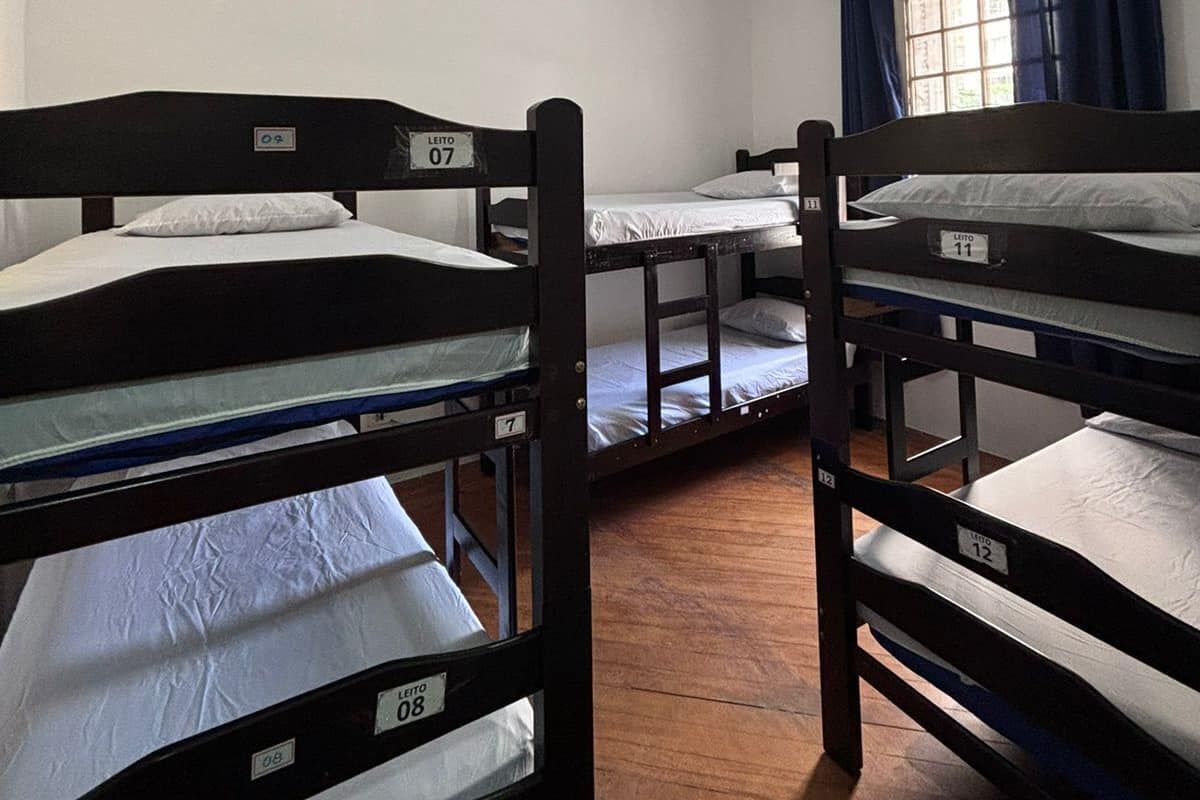 Ein Schlafsaalzimmer mit Stockbetten, nummeriert von 07 bis 12, einem Fenster mit Vorhängen und einer Deckenleuchte.