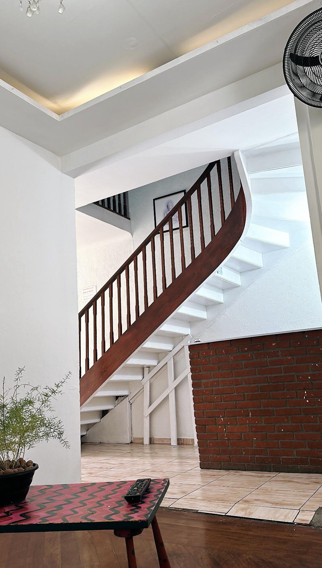 A staircase with a wooden handrail leading to a balcony with a brick wall.