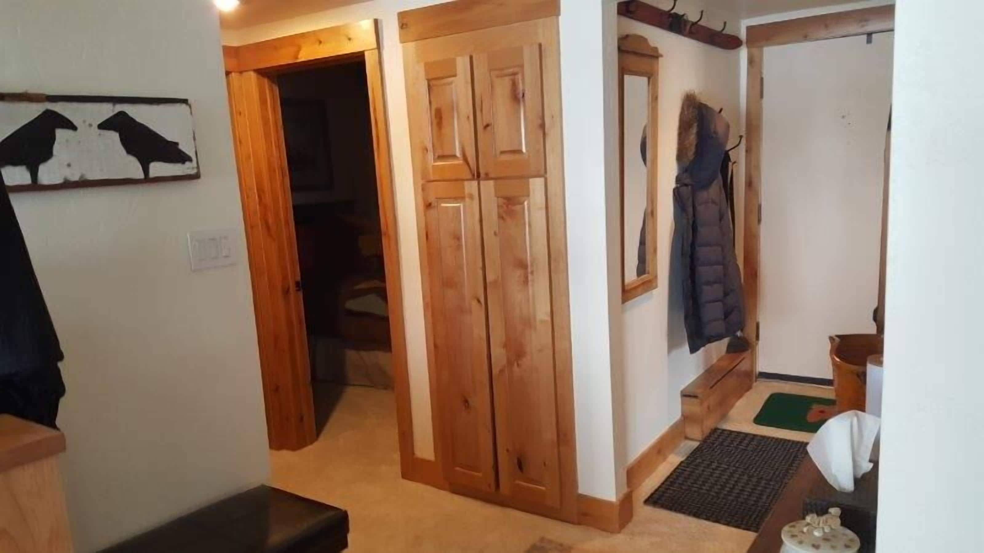 Un couloir avec des portes en bois, un porte-manteau et un banc.