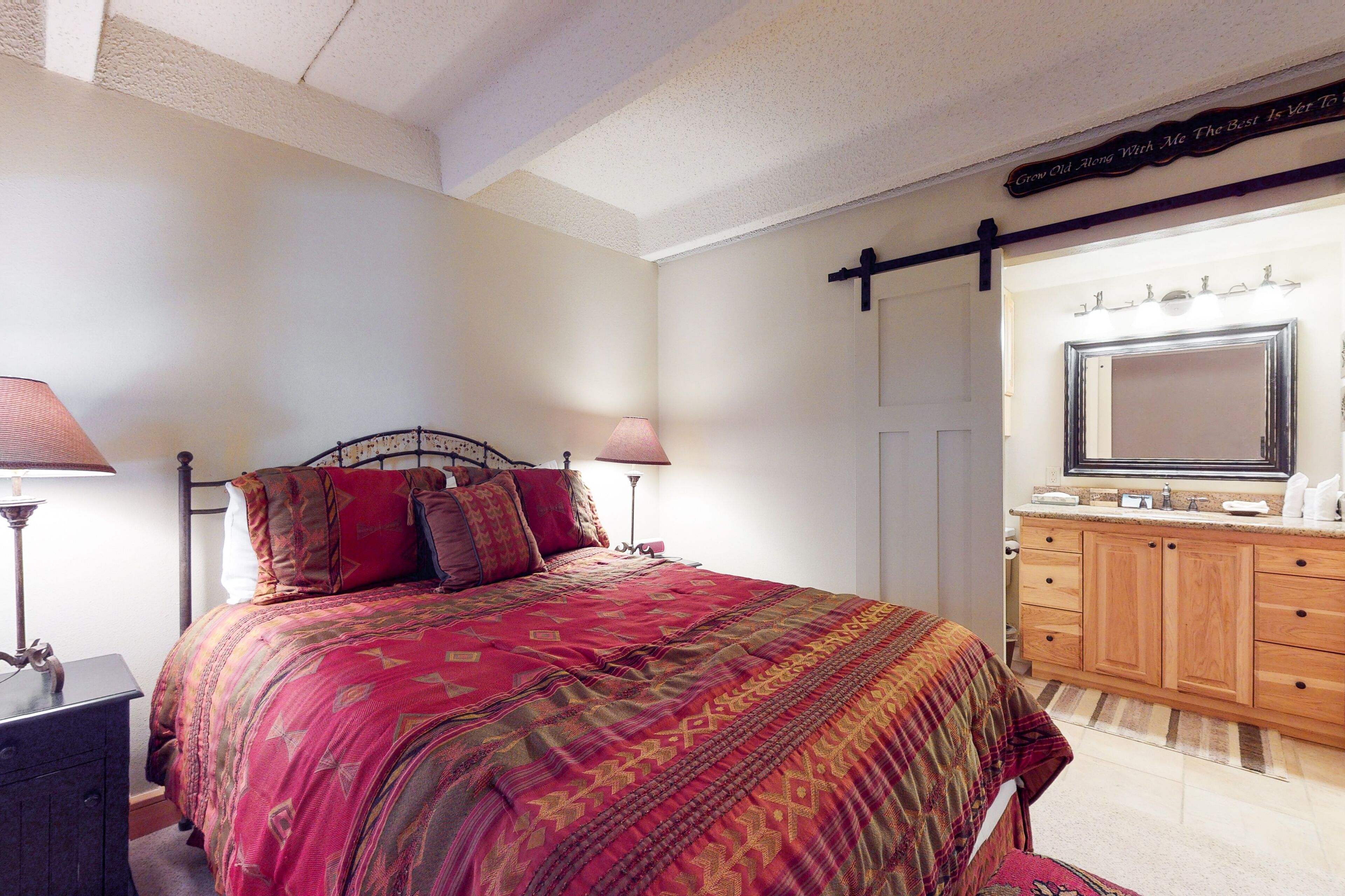 A bedroom with a large bed, a wooden dresser with a mirror, and a wall-mounted light fixture.