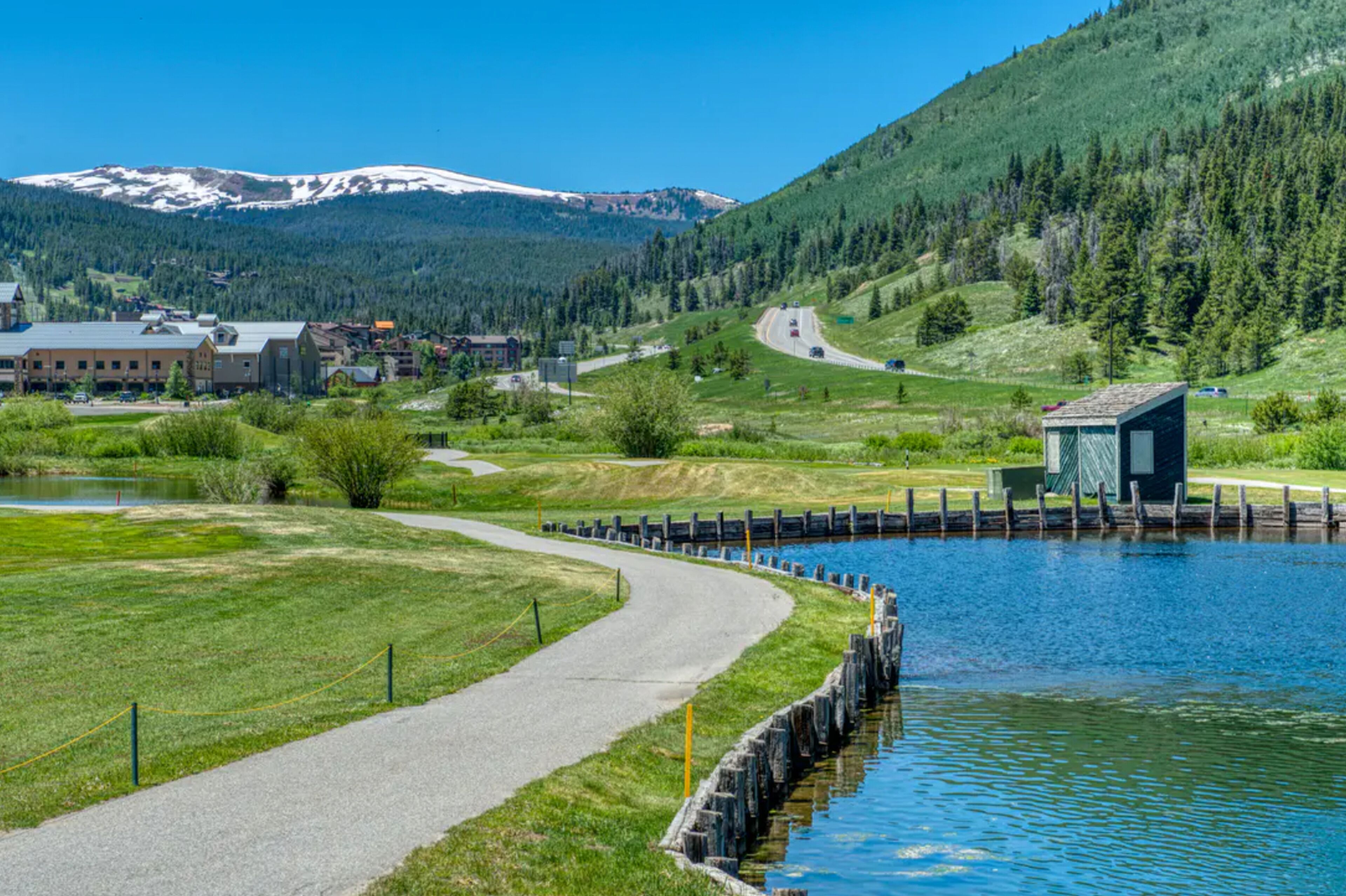 Une vue sur le lac, avec un sentier pavé, un petit quai et des bâtiments en arrière-plan.