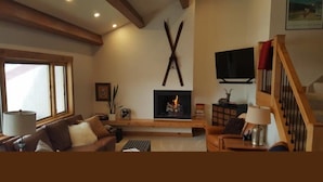 Uma sala de estar aconchegante com lareira, vigas de madeira, televisão e escada.