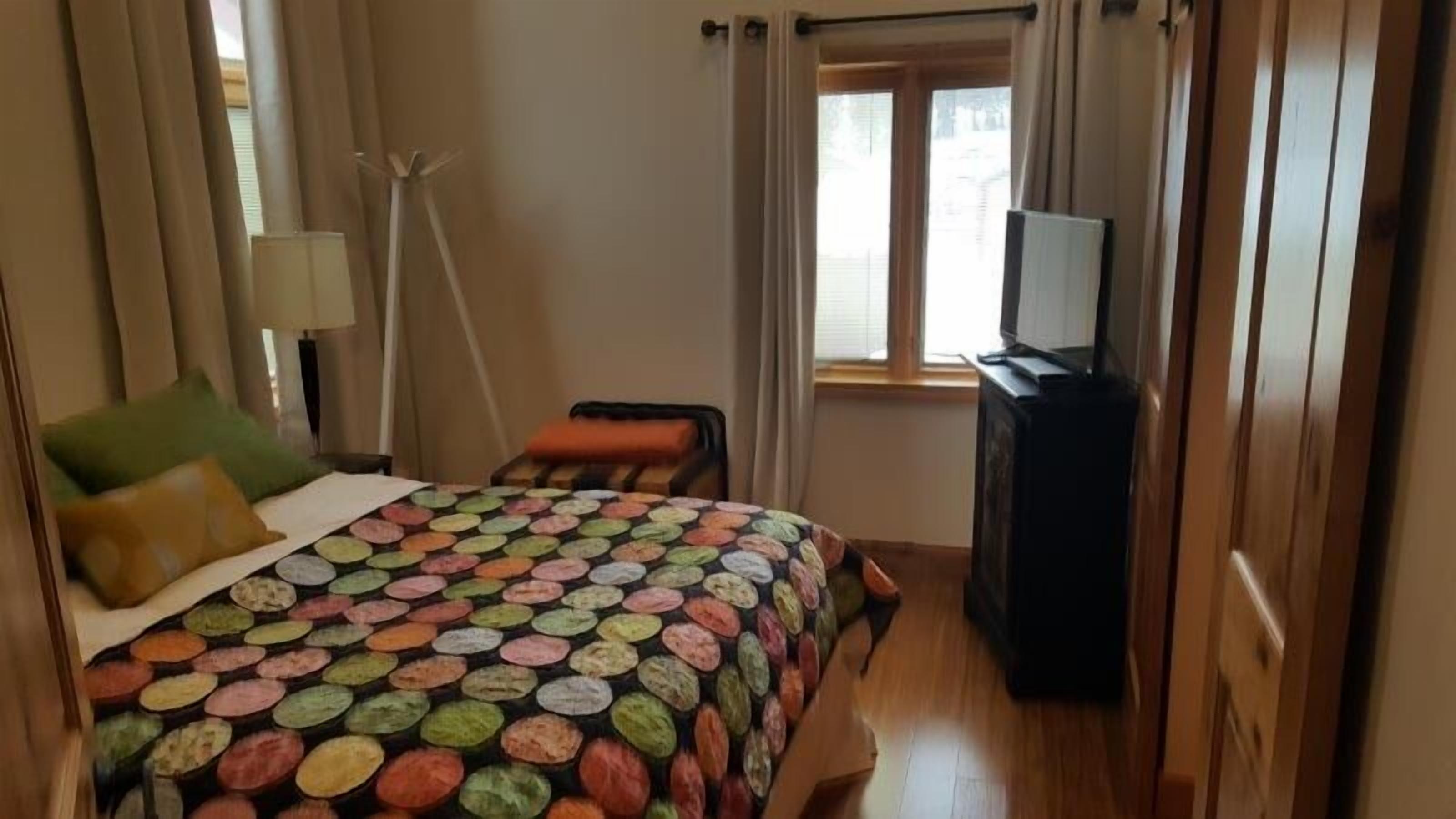 A hotel room with a bed, a chair, a TV, and a window with curtains.
