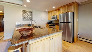 Uma cozinha moderna com bancadas de granito, armários de madeira, eletrodomésticos de aço inoxidável e um detalhe decorativo na parede.