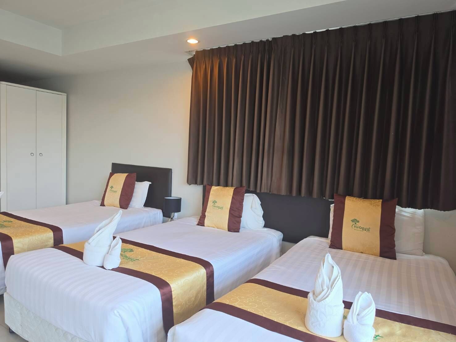 A hotel room with four beds, each with a headboard and pillows, and a large window with curtains.