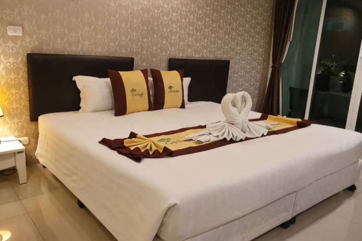 Quarto de hotel com uma cama grande, cabeceira e janela com cortinas.