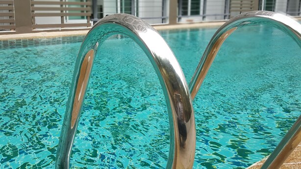 Una piscina con agua cristalina y escaleras metálicas.