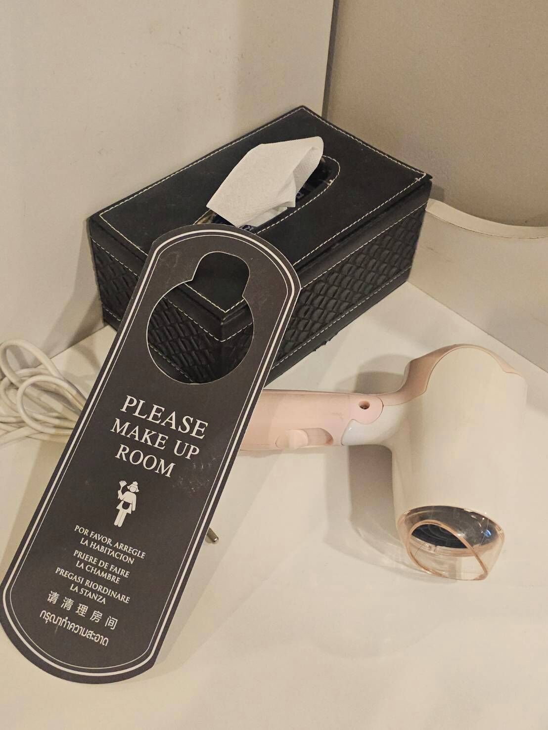 Ein Taschentuchhalter und ein Taschentuchspender mit einem Schild, auf dem 'PLEASE MAKE UP ROOM' in verschiedenen Sprachen steht.