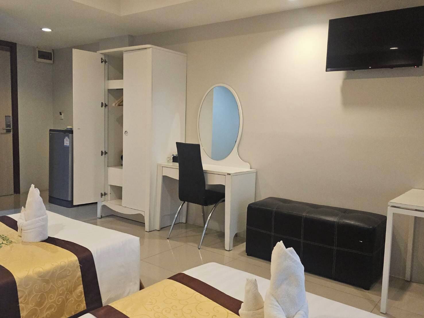 Ein Hotelzimmer mit zwei Betten, einem Schreibtisch mit Stuhl, einem Kleiderschrank, einem Fernseher und einem kleinen Kühlschrank.