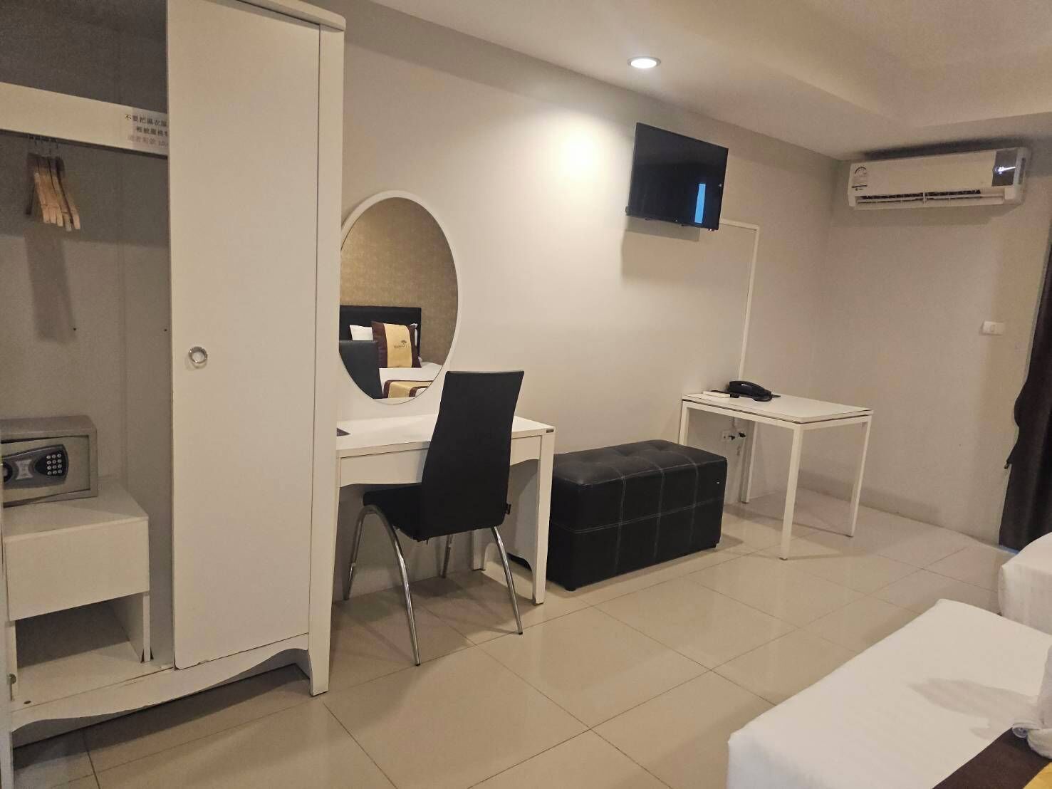 A hotel room with a desk, chair, bedside table, and a TV mounted on the wall.