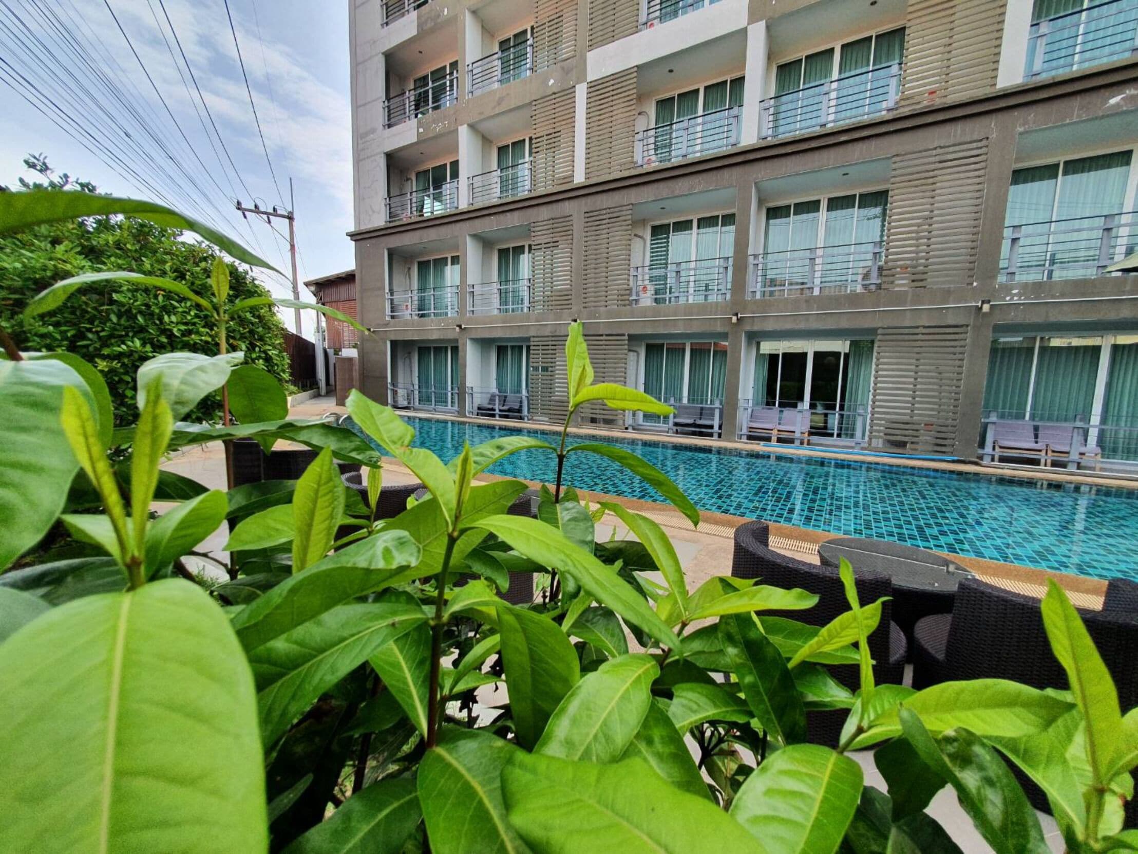 A hotel with a swimming pool, multiple balconies, and lush greenery.