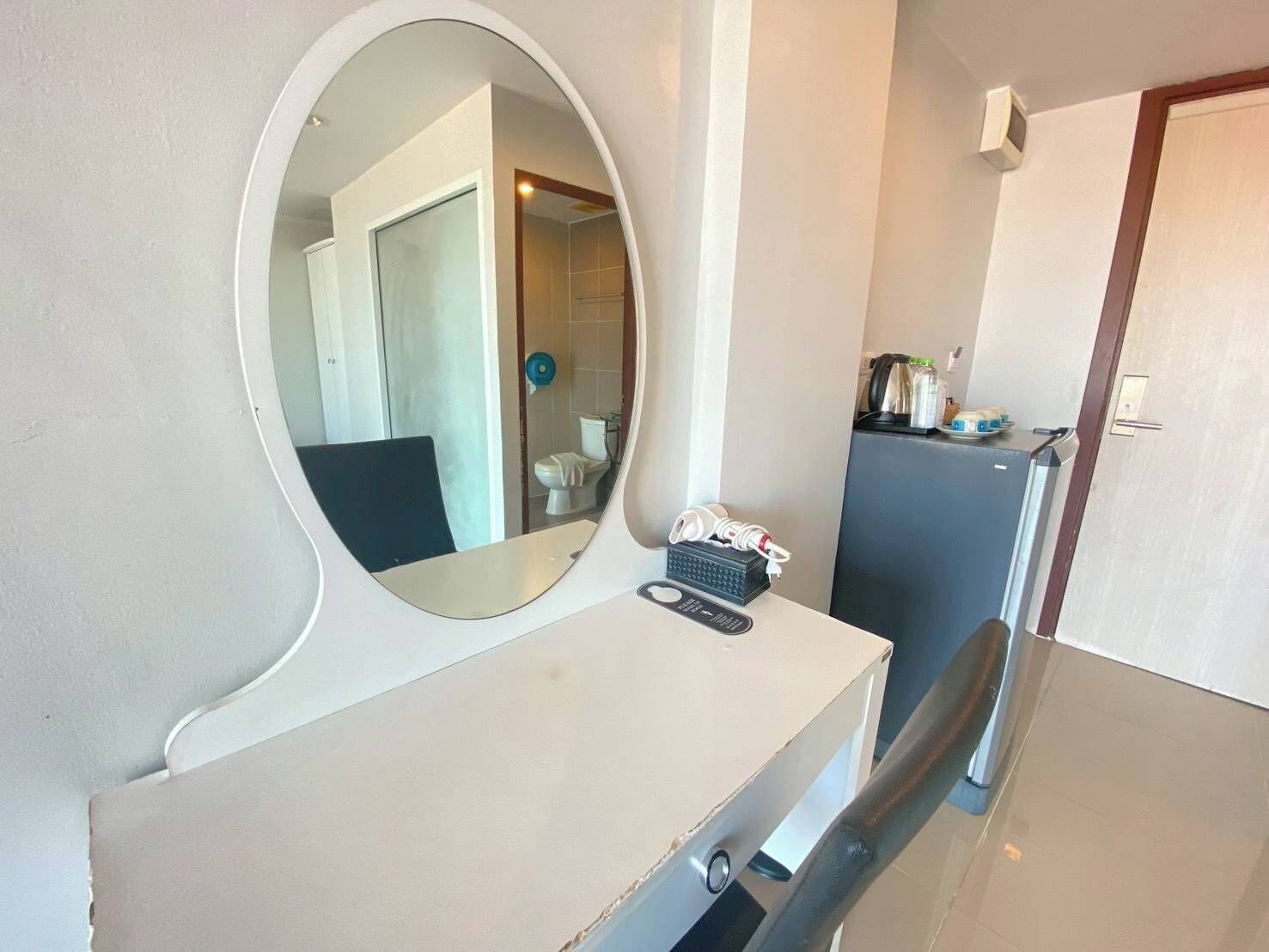 Une petite pièce comprenant un bureau, une chaise, un miroir et une porte.