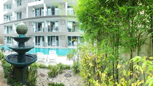 Un jardín con una fuente, una piscina y un edificio de varios pisos al fondo.