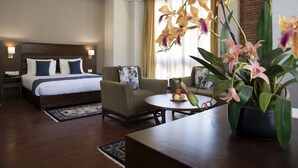 Una habitación de hotel con cama, sofá, una mesita con fruta y una orquídea en maceta.