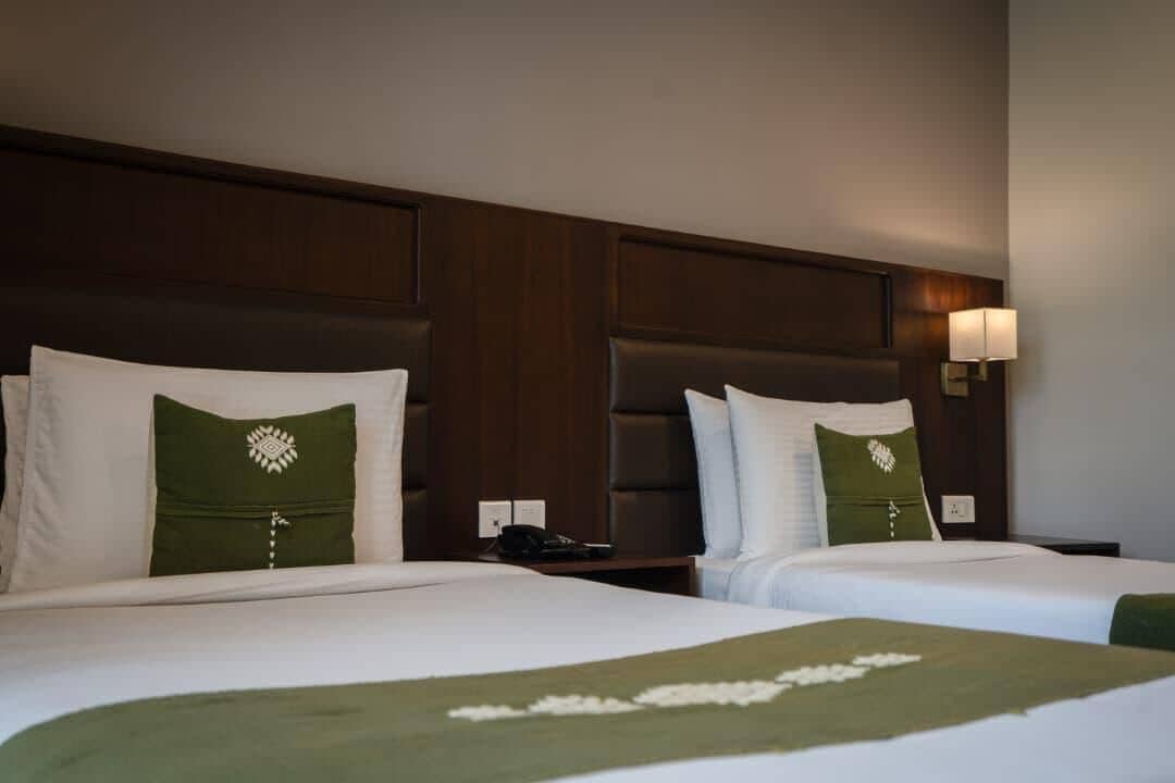 Habitación de hotel con dos camas, cada una con una almohada y una mesita de noche.