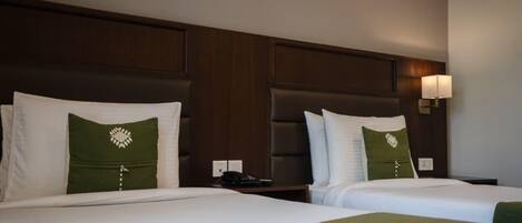 A hotel room with two beds, each with a pillow and a bedside table.