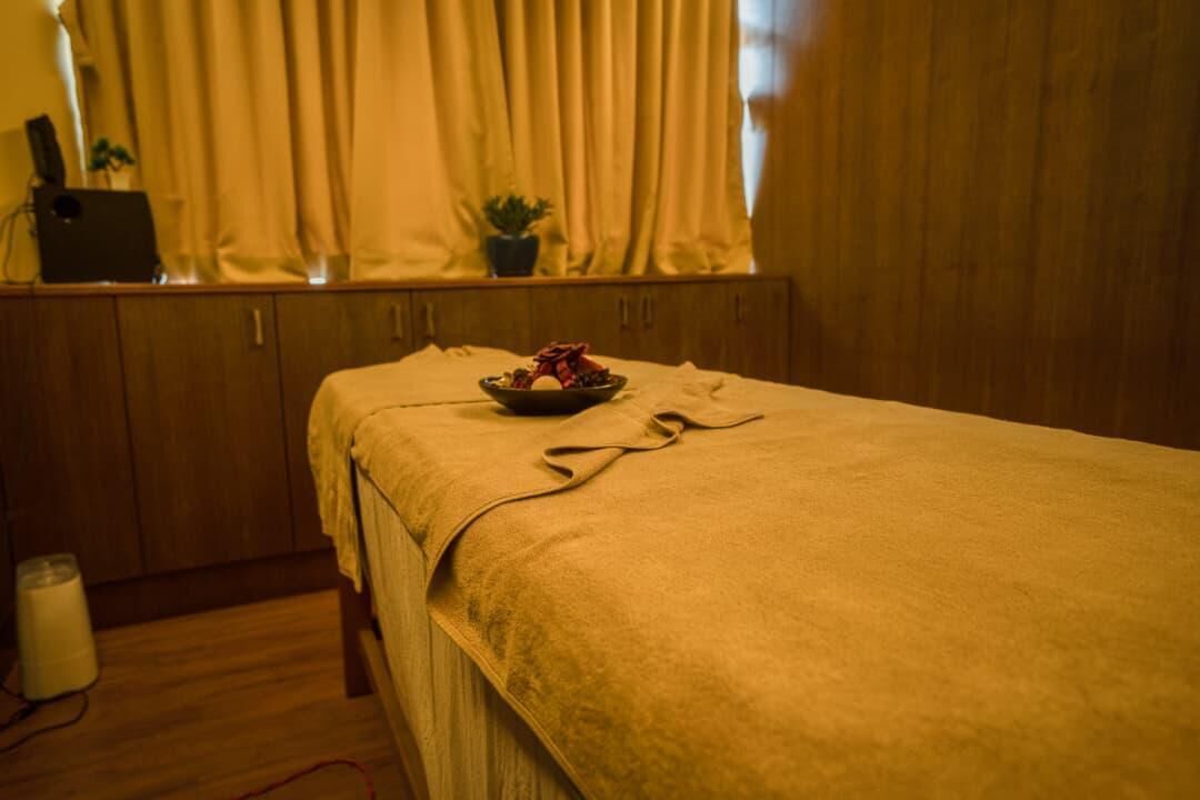 Une pièce avec un lit, une fenêtre avec des rideaux, une petite table avec un bol et une plante en pot.