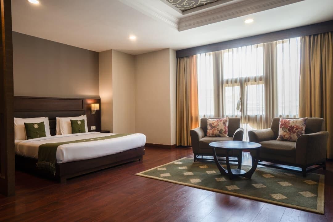 A hotel room with a bed, a sofa, a coffee table, and a window with curtains.
