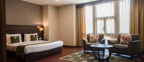 A hotel room with a bed, a sofa, a coffee table, and a window with curtains.