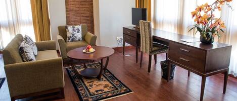 Una sala de estar con sofá, sillón, mesa de centro, mueble para televisión y escritorio con silla.
