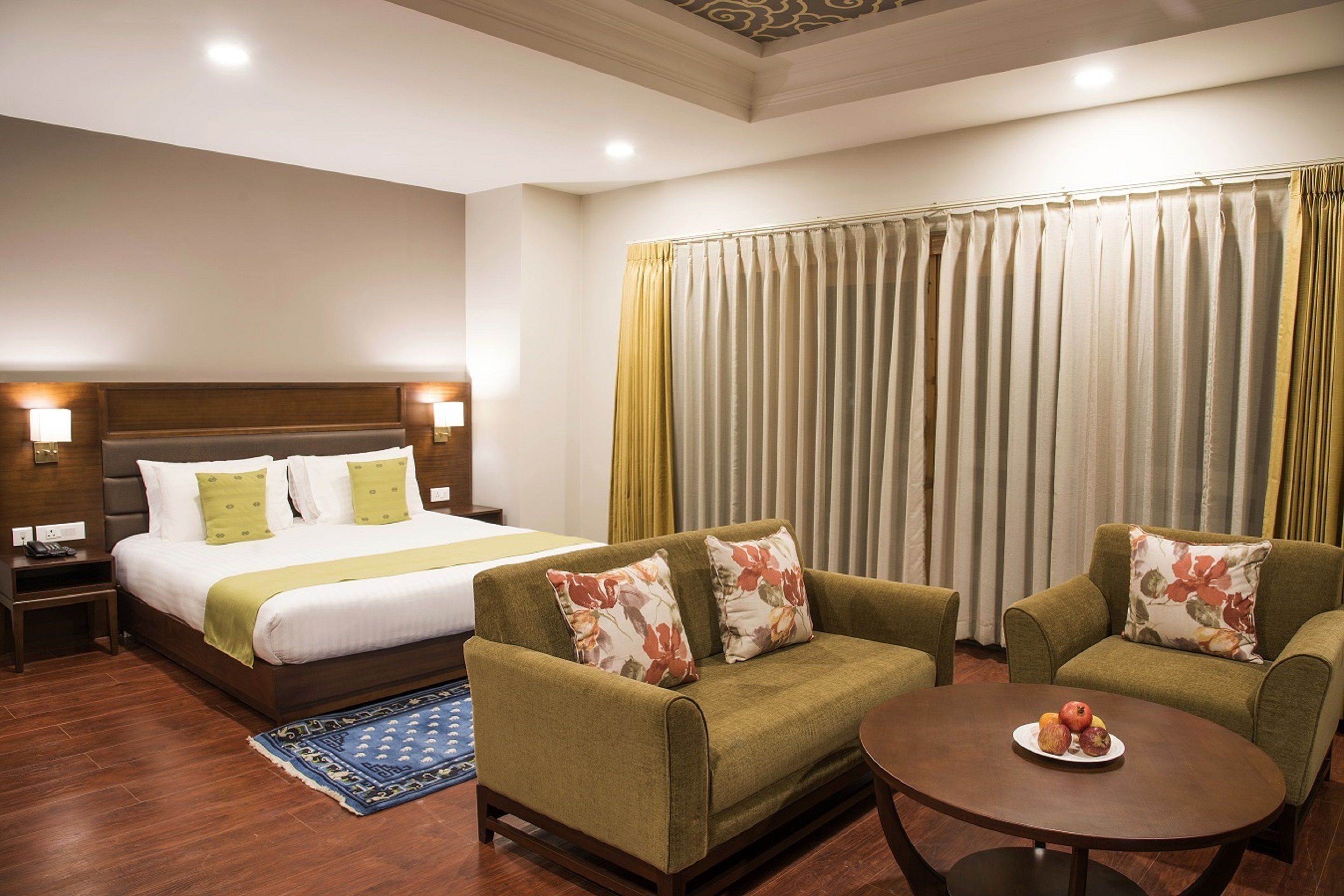 A hotel room with a bed, two armchairs, a small table with fruit, and a window with curtains.