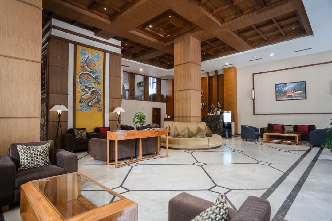 Een ruime lobby met een modern design, een centraal zitgedeelte met banken en een salontafel, een grote decoratieve wand met een draken schilderij, en een receptiebalie.