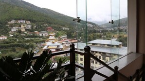 Vista desde un balcón con barandilla de cristal, sobre un pueblo con edificios y una montaña al fondo.