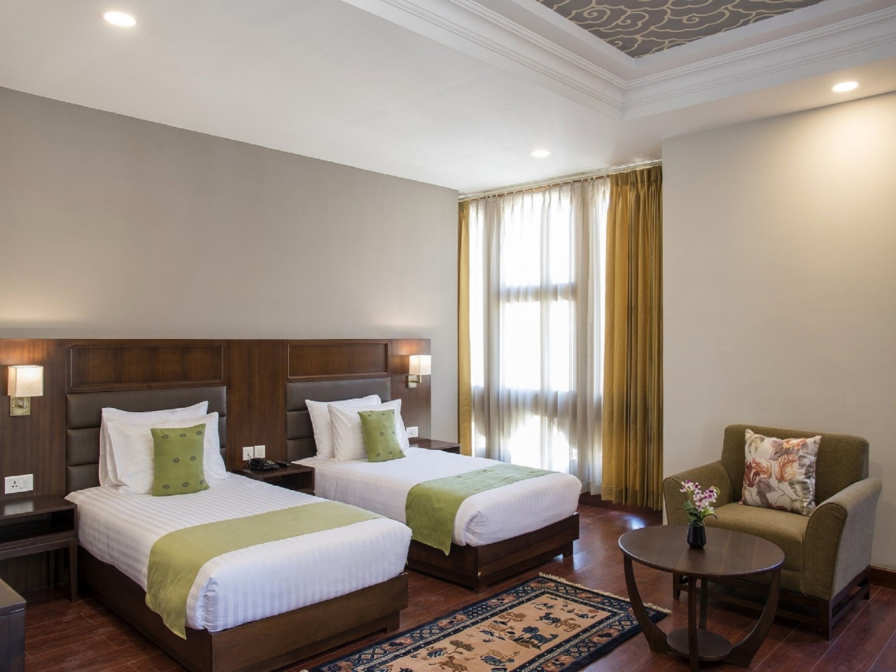 Habitación de hotel con dos camas, un sofá, una mesita y una ventana con cortinas.