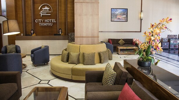 Un vestíbulo de hotel con mostrador de recepción, sofás, una mesa de centro y una planta grande en maceta.